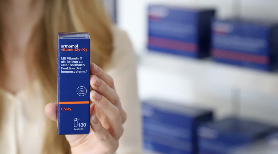 Frau hält Orthomol Vitamin D3+K2 Spray-Verpackung. Blaue Schachtel.